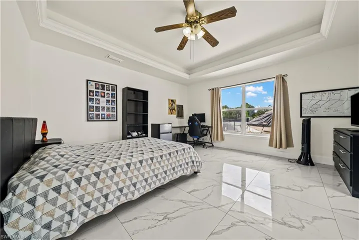 Bedroom with a tray ceiling, ceiling fan, ornamental molding, and light marble finish floors