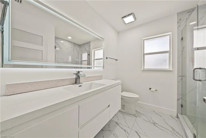 Bathroom featuring vanity, a marble finish shower, and light marble finish floors