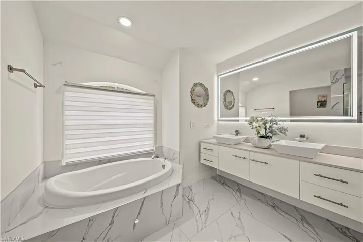 Full bath with double vanity, recessed lighting, a bath, and light marble finish floors