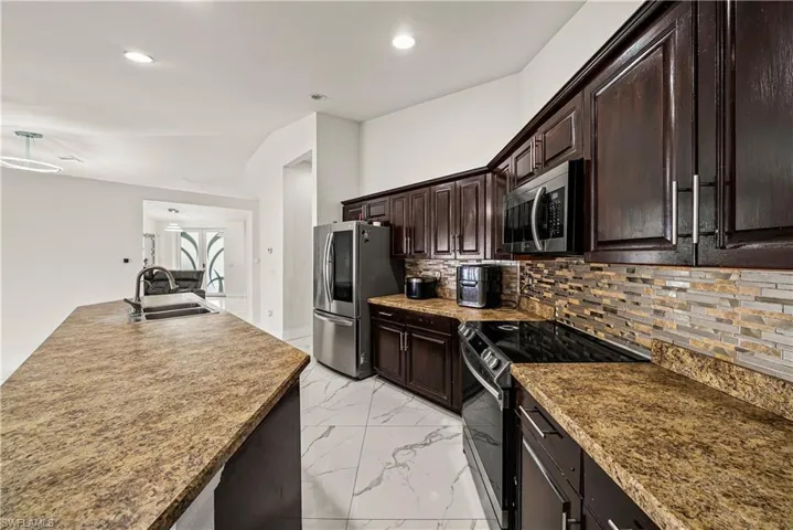 Kitchen featuring dark wood finish cabinetry, stainless steel appliances, light marble finish flooring, recessed lighting, and decorative backsplash