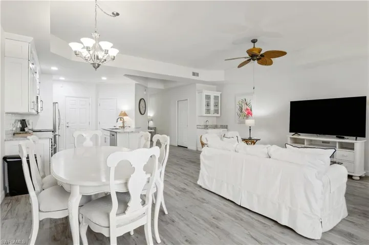 Dining area with light wood-style floors, ceiling fan with notable chandelier, visible vents, and recessed lighting