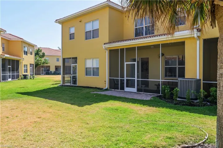 Rear view of property featuring a sunroom, stucco siding, a yard, and central AC