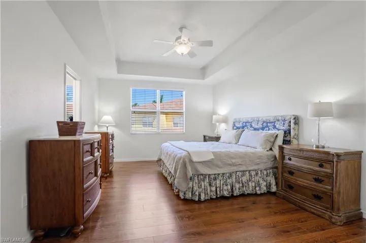 Bedroom featuring dark wood-style flooring, a raised ceiling, baseboards, and ceiling fan