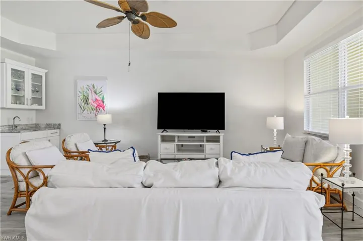 Living room with a ceiling fan, light wood-style flooring, and a raised ceiling