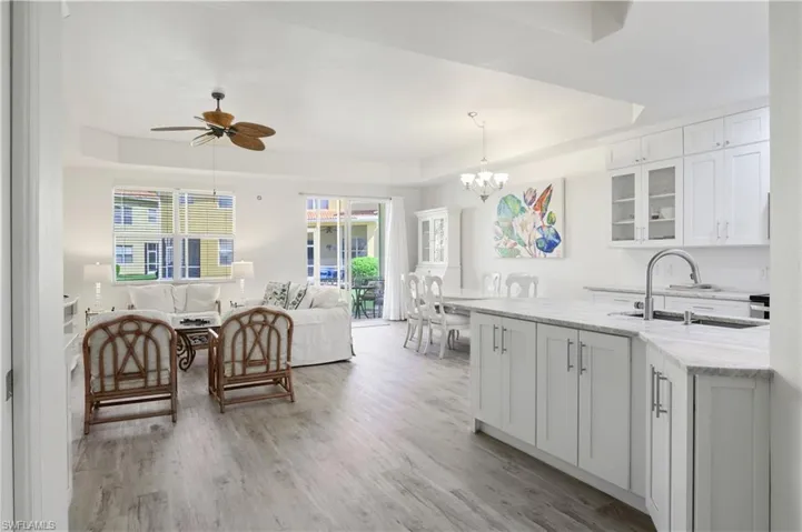 Kitchen featuring a sink, white cabinetry, light wood-type flooring, light stone countertops, and a raised ceiling
