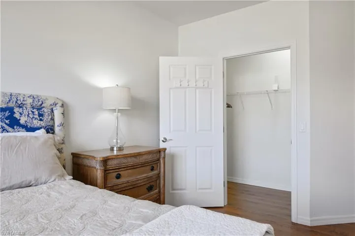 Bedroom with a walk in closet, a closet, baseboards, vaulted ceiling, and wood finished floors