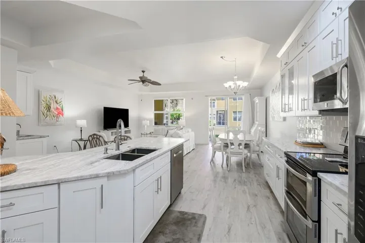 Kitchen with a sink, ceiling fan with notable chandelier, open floor plan, a raised ceiling, and stainless steel appliances