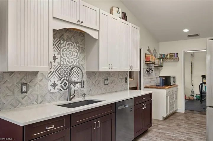 Kitchen with sink, dark brown cabinets, light hardwood / wood-style floors, white cabinets, and stainless steel dishwasher