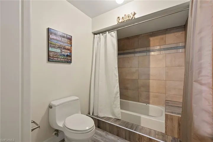 Bathroom with hardwood / wood-style flooring, shower / bath combo, and toilet