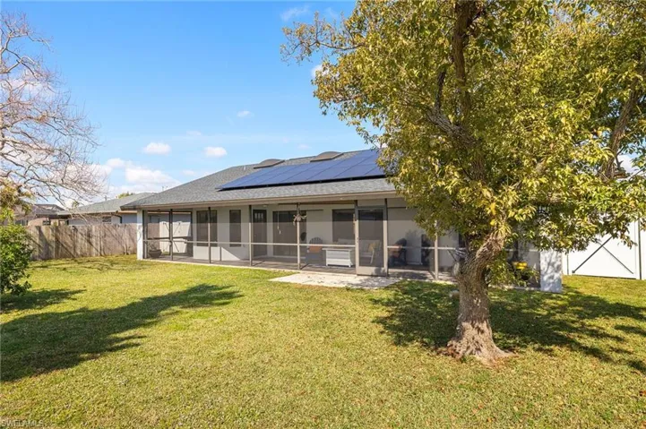 Rear view of property featuring a patio, a yard, a sunroom, and solar panels