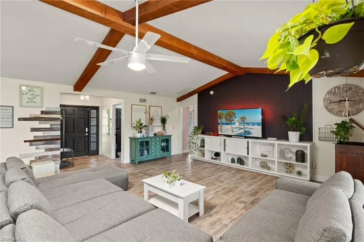 Living room featuring ceiling fan, wood-type flooring, wooden walls, and vaulted ceiling with beams