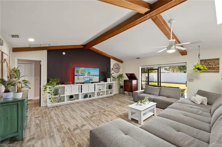 Living room featuring wood-type flooring, vaulted ceiling with beams, wooden walls, and ceiling fan