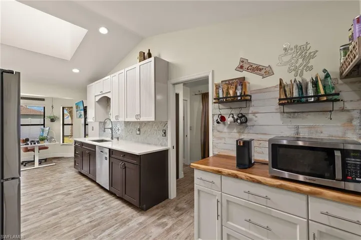 Kitchen featuring lofted ceiling with skylight, sink, white cabinetry, appliances with stainless steel finishes, and decorative backsplash