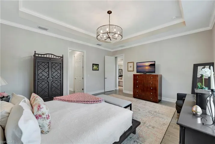 Bedroom with ornamental molding, a notable chandelier, light hardwood / wood-style floors, and a tray ceiling