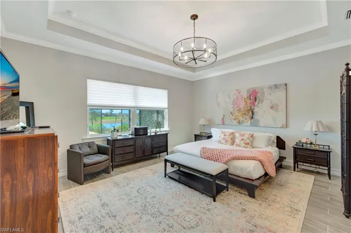 Bedroom featuring a raised ceiling, crown molding, an inviting chandelier, and light hardwood / wood-style floors