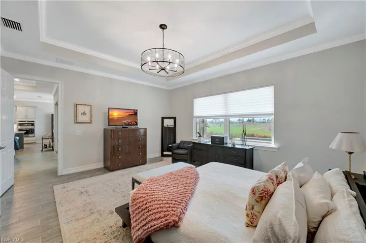 Bedroom featuring ornamental molding, light hardwood / wood-style flooring, a notable chandelier, and a tray ceiling
