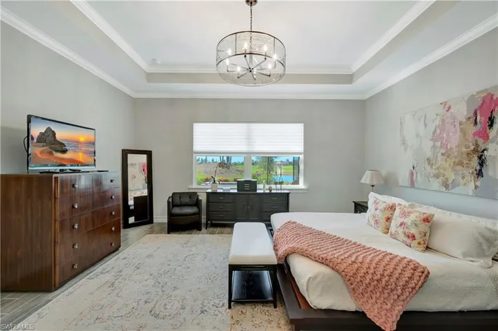 Bedroom featuring a raised ceiling, ornamental molding, a notable chandelier, and light hardwood / wood-style floors