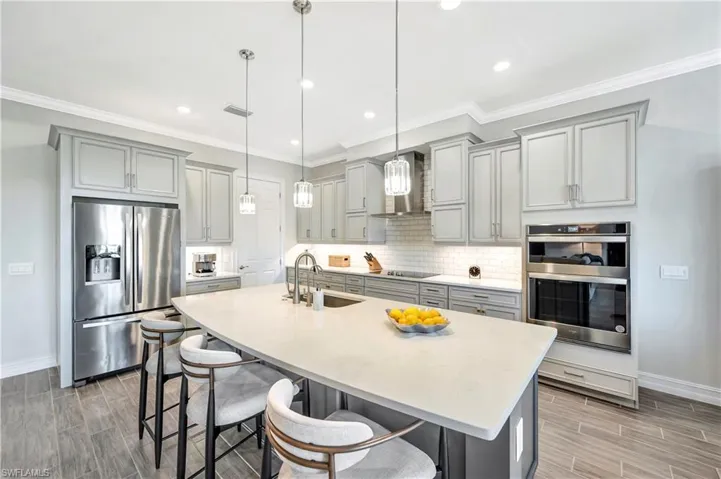 Kitchen with wall chimney exhaust hood, sink, appliances with stainless steel finishes, a kitchen breakfast bar, and pendant lighting