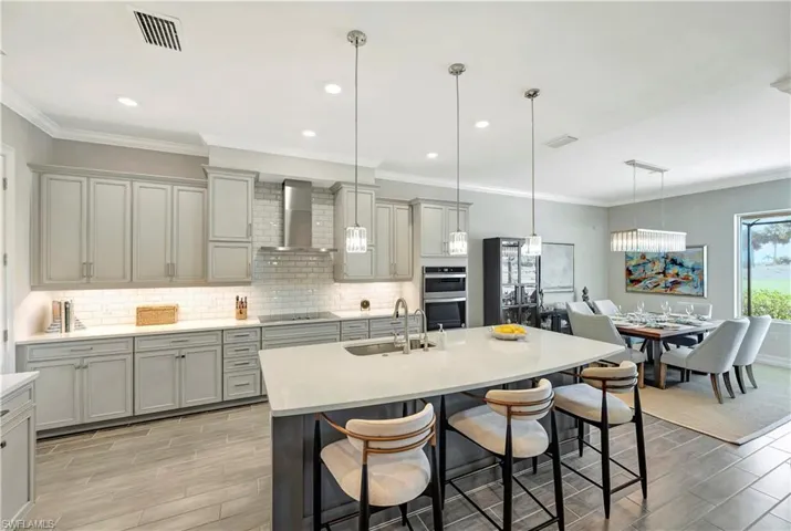 Kitchen with wall chimney exhaust hood, sink, hanging light fixtures, black electric cooktop, and a kitchen breakfast bar
