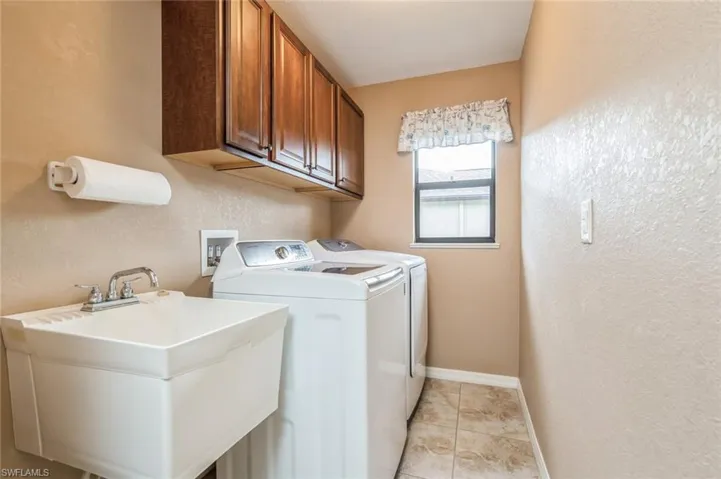 Laundry area featuring independent washer and dryer, washer hookup, light tile floors, sink, and cabinets