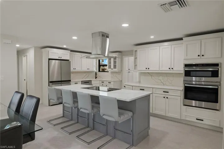 Kitchen with large island, white & gray cabinetry, island exhaust hood, and stainless steel appliances
