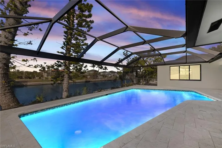 Pool at dusk featuring a water view, a patio area, and a lanai