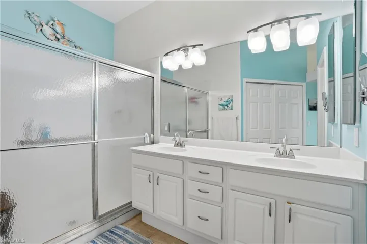 Bathroom featuring a shower stall, double vanity, and light tile patterned flooring