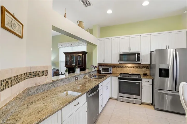 Kitchen featuring light stone countertops, appliances with stainless steel finishes, white cabinetry, decorative backsplash, and recessed lighting