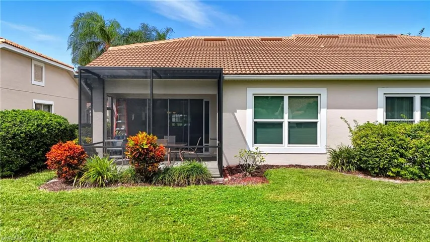 Rear view of property with a sunroom, a lawn, a tile roof, stucco siding, and glass enclosure