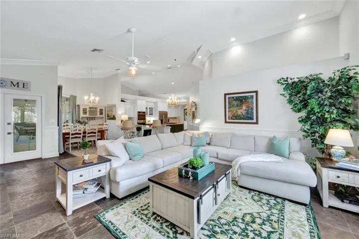Living room with ceiling fan with notable chandelier, ornamental molding, and vaulted ceiling