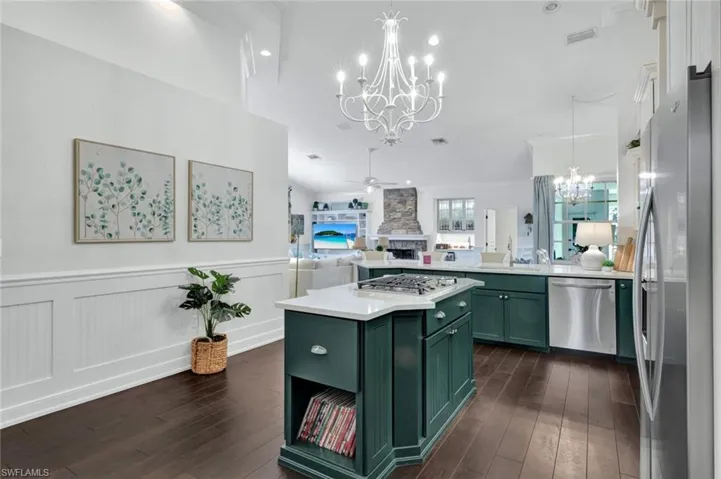 Kitchen featuring ceiling fan with notable chandelier, stainless steel appliances, a fireplace, open floor plan, and green cabinetry