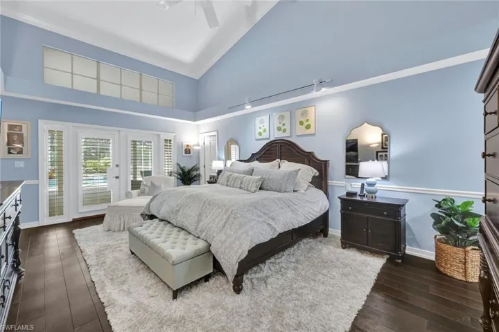 Bedroom with ceiling fan, access to exterior, dark hardwood / wood-style floors, and high vaulted ceiling