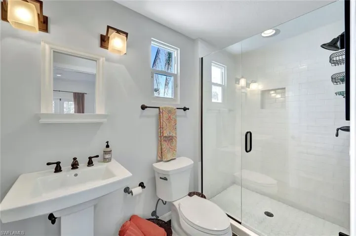 Bathroom featuring toilet, sink, and a shower with shower door