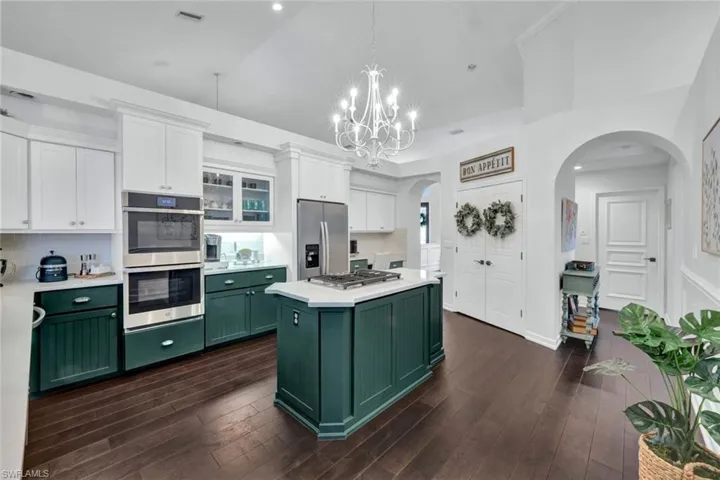 Kitchen with white cabinets, dark wood-style flooring, stainless steel appliances, light countertops, and green cabinets