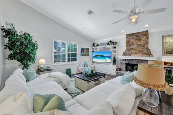Living room featuring a stone fireplace, ceiling fan, lofted ceiling, wood-type flooring, and ornamental molding