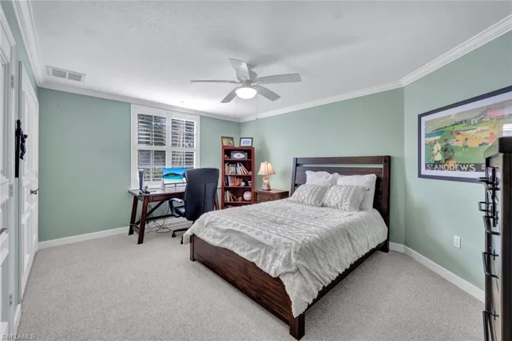 Carpeted bedroom with ceiling fan and crown molding