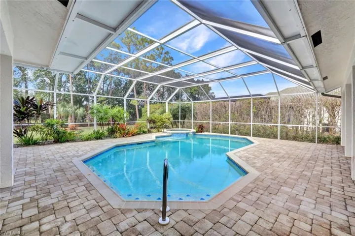 View of swimming pool featuring a patio area, glass enclosure, and an in ground hot tub