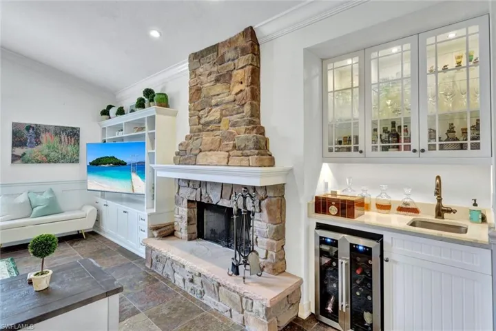 Bar with a fireplace, sink, white cabinetry, ornamental molding, and beverage cooler