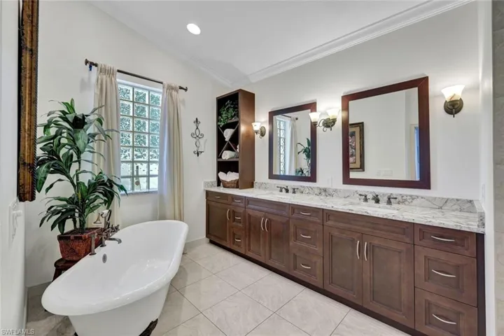 Bathroom with lofted ceiling, tile patterned floors, vanity, a washtub, and crown molding