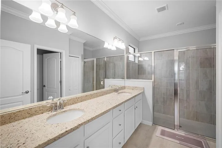 Full bath with a shower stall, double vanity, ornamental molding, and a closet