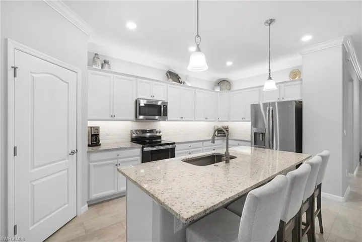 Kitchen featuring backsplash, white cabinetry, a breakfast bar, stainless steel appliances, and ornamental molding