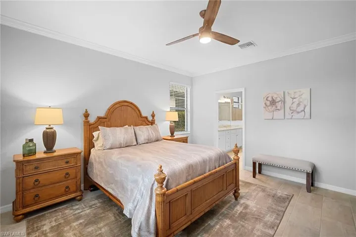 Tiled bedroom with crown molding, ceiling fan, and ensuite bath