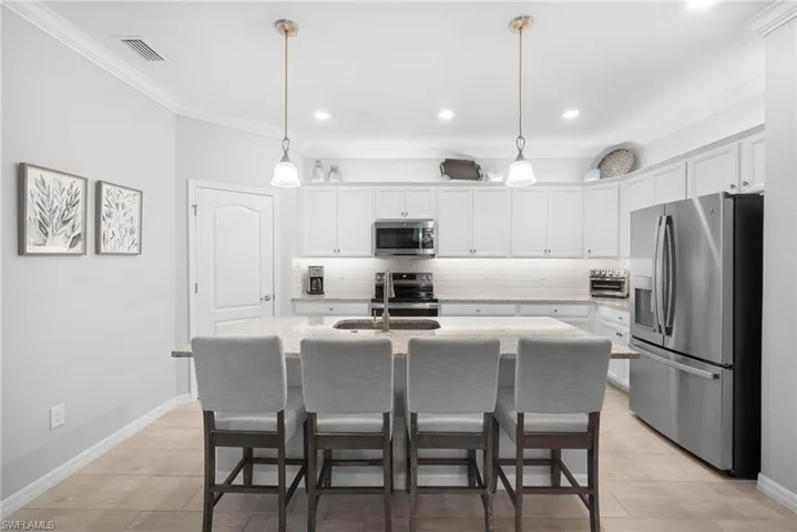 Kitchen featuring a kitchen bar, tasteful backsplash, stainless steel appliances, white cabinets, and ornamental molding