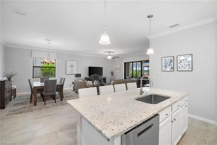 Kitchen with white cabinets, light stone countertops, decorative light fixtures, and ornamental molding