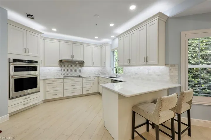 Kitchen with light stone countertops, white cabinetry, a breakfast bar, a peninsula, and recessed lighting
