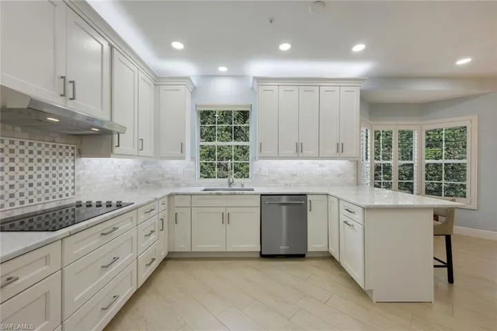 Kitchen with a peninsula, decorative backsplash, recessed lighting, dishwasher, and light stone counters