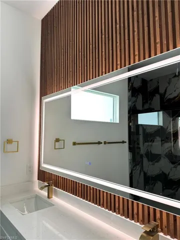 Bathroom vanity featuring a quartz countertop with an integrated sink, illuminated mirror, and a brass-finish faucet