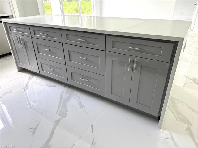 Expansive kitchen island featuring a light gray shaker cabinet base, modern silver-tone hardware, and a solid light-toned countertop