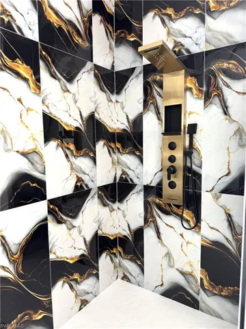 Shower enclosure featuring black, white, and gold marble-patterned wall tiles