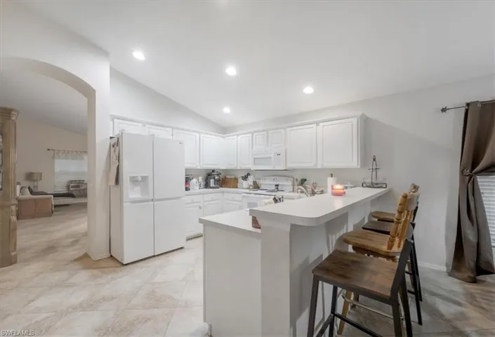Kitchen with a kitchen bar, white appliances, kitchen peninsula, lofted ceiling, and light tile patterned flooring